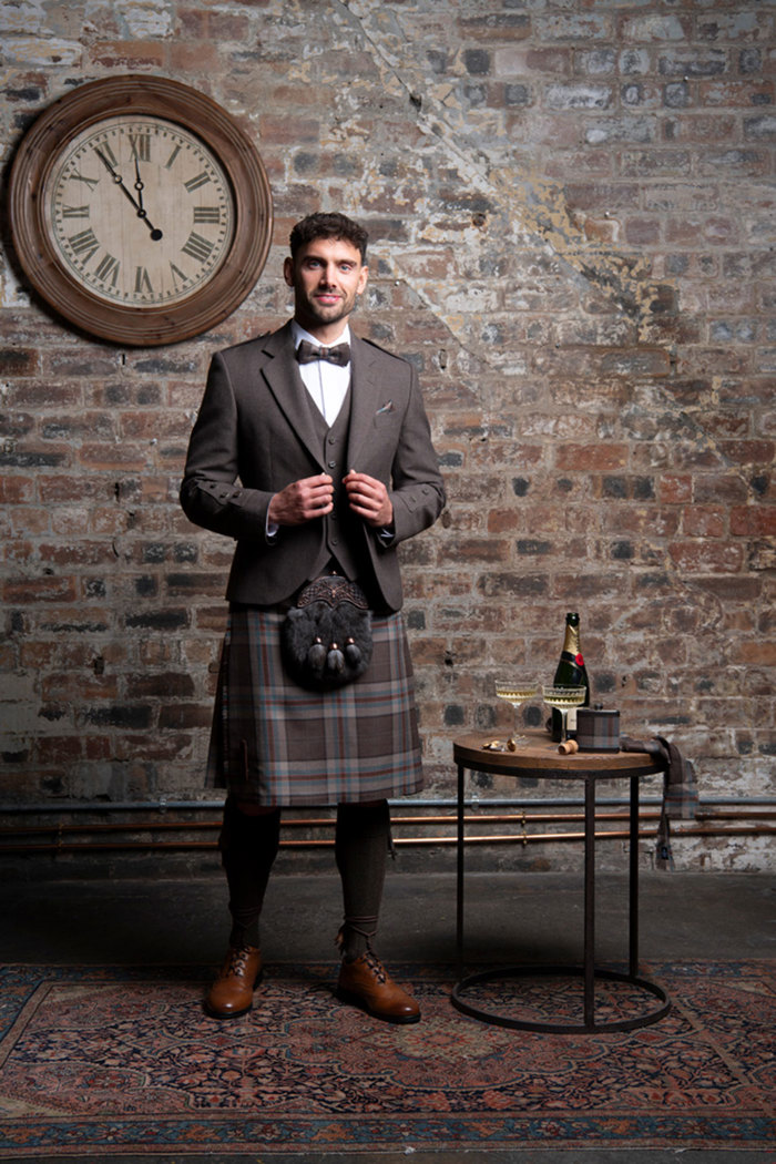 A person wearing a Jura Mist tartan kilt outfit from MacGregor and MacDuff featuring brown, red and green checked kilt.