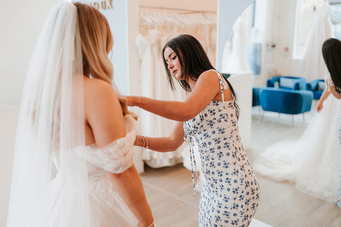 a brunette woman in floral dress taking measurements of a woman in wedding dress and veil