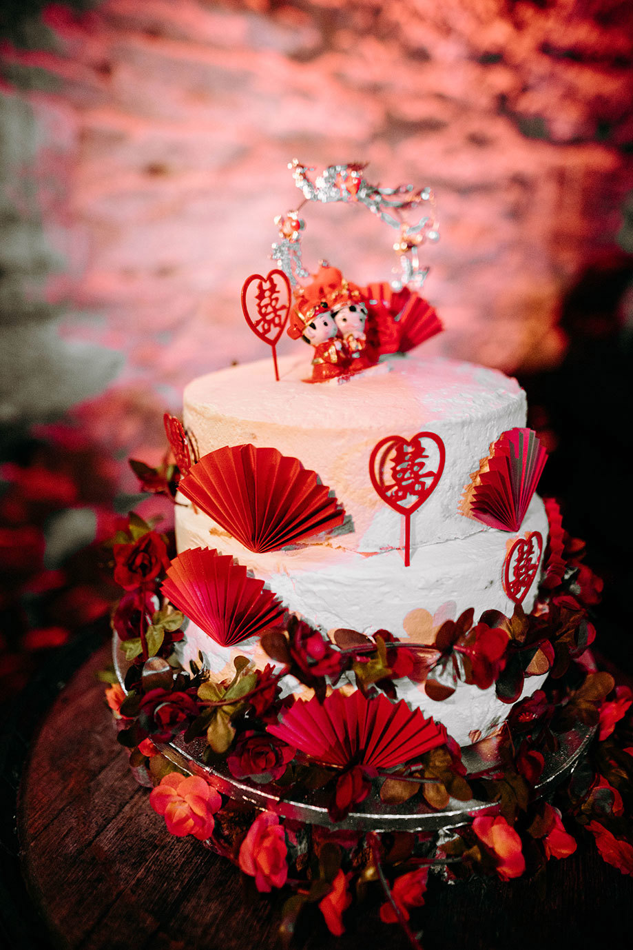 a tiered cake decorated with small red fans and heart decorations