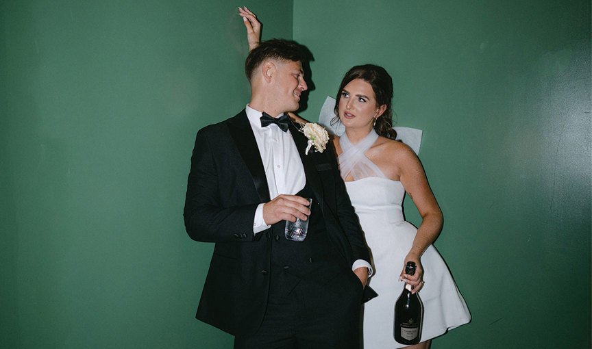 a bride and groom leaning against a green wall