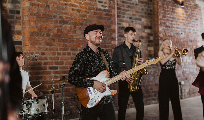 a group of people playing musical instruments standing against a red brick wall