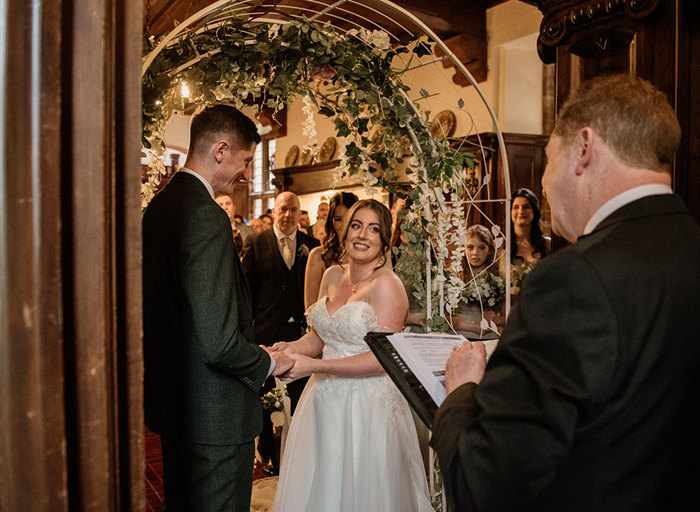 A bride and groom during their wedding ceremony standing underneath a flower arch