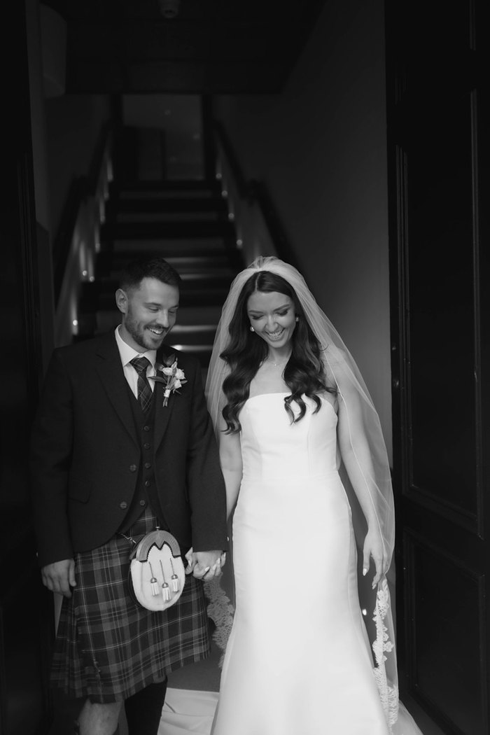 A black and white photo of a bride and groom holding hands and walking down a staircase