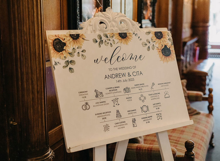 A white wedding welcome sign on an easel stand with a sunflower design 