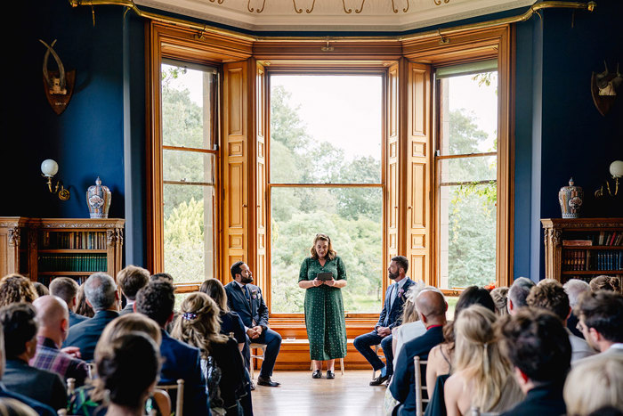 Celebrant stands between two seated grooms during wedding ceremony