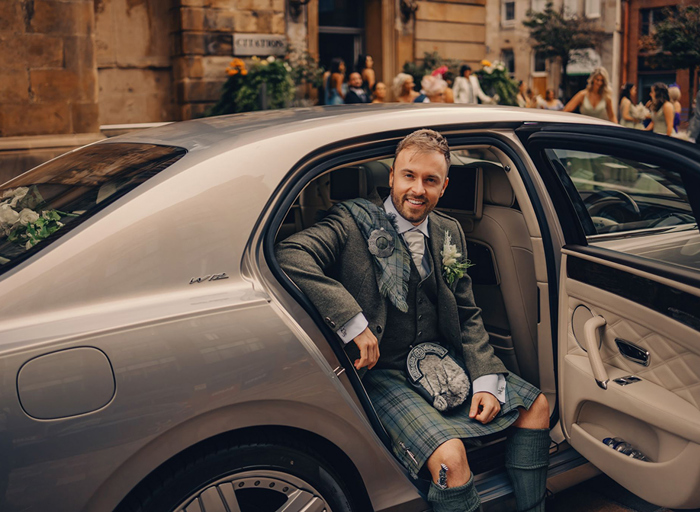 groom wearing highlandwear getting out of car and smiling