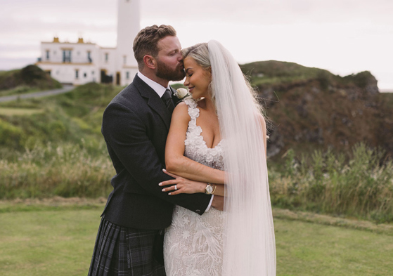 Groom kisses brides forehead as they pose in outdoor photoshoot