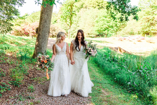 Two Brides Walking Hand In Hand In A Garden