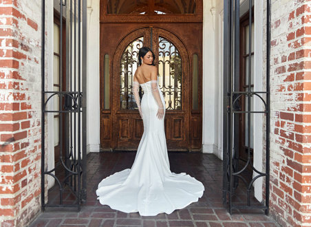 bride looks over her shoulder while stood in front of large wooden door wearing a strapless trailing wedding dress and long tulle gloves