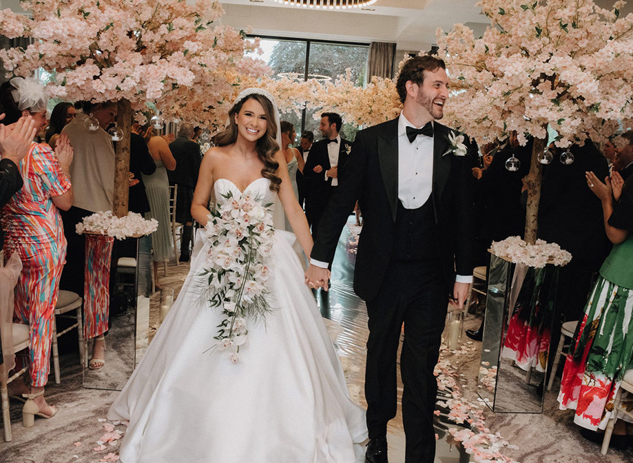 a bride and groom walking up the aisle at Cameron House with cherry blossom trees either side.