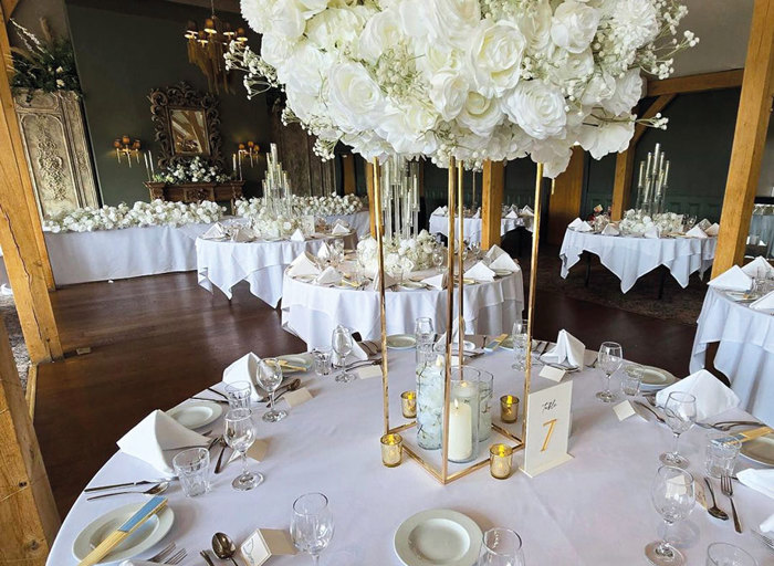 round tables dressed with abundant white roses in a room set for a wedding dinner