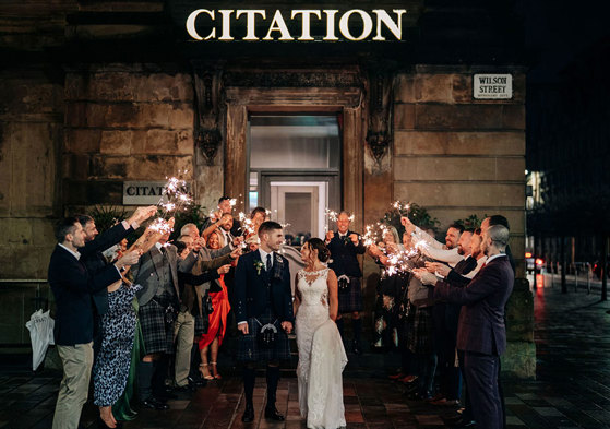 A bride and groom looking at each other as they walk through a crowd of people holding sparklers