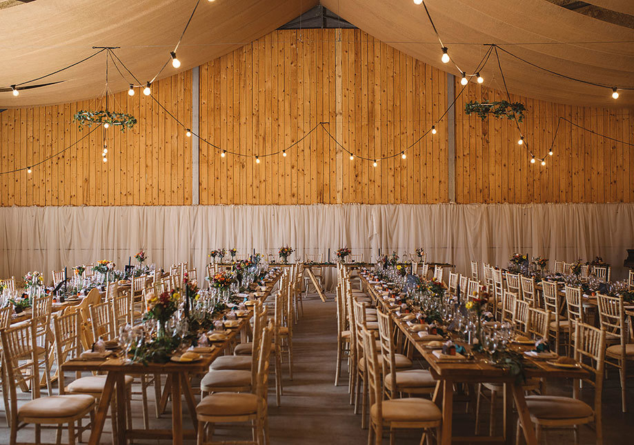 The Barn at Carrick Castle with wooden clad walls, set with long tables and chiavari chairs for a wedding dinner