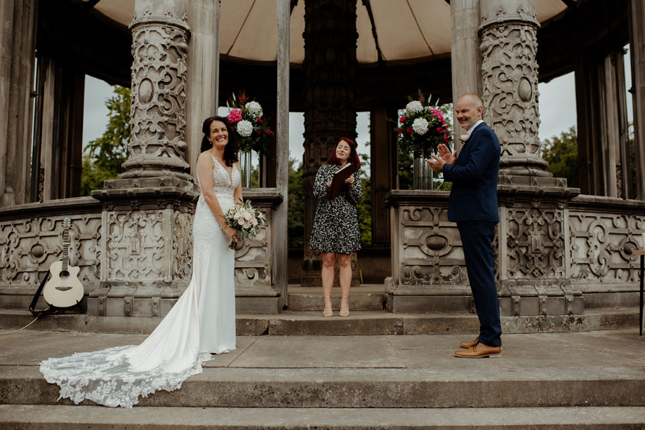 Bride holds bouquet and groom claps his hands during ceremony