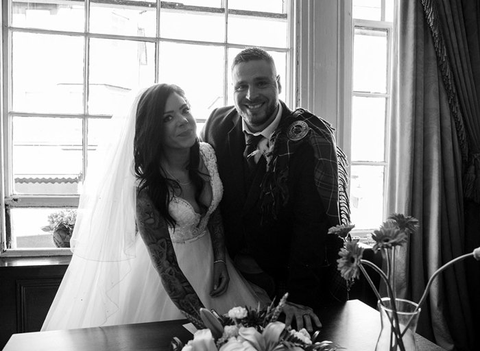 A black and white photo of a bride and groom standing at a table signing their marriage license 