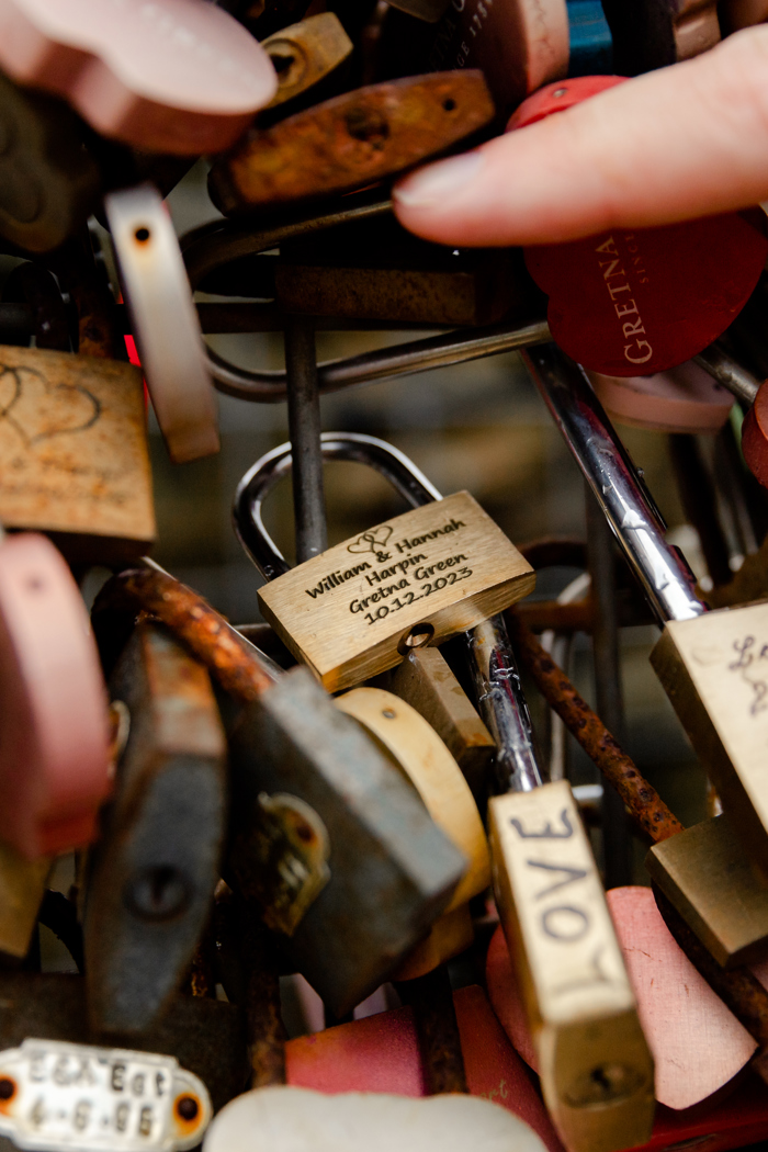 bride and groom put personalised padlock on bridge at gretna green