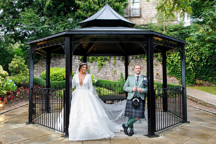 a bride and groom standing in a black Victorian bandstand in a garden.