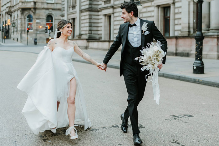 A bride and groom walk through a city holding hands 