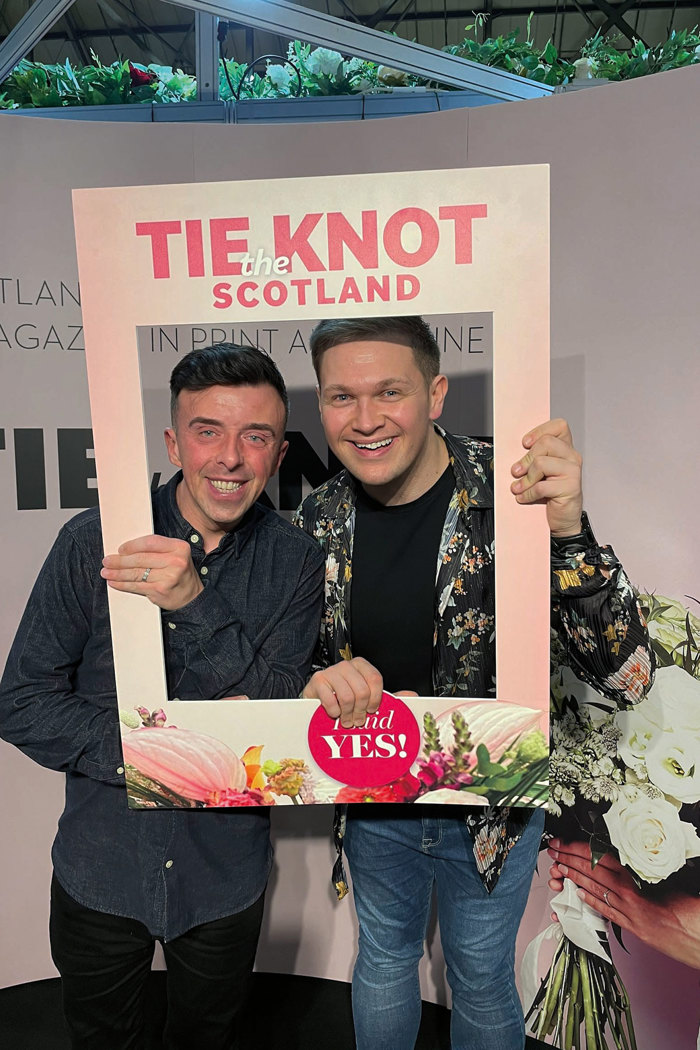 Two men holding a cardboard sign that looks like a magazine and smiling at the camera 