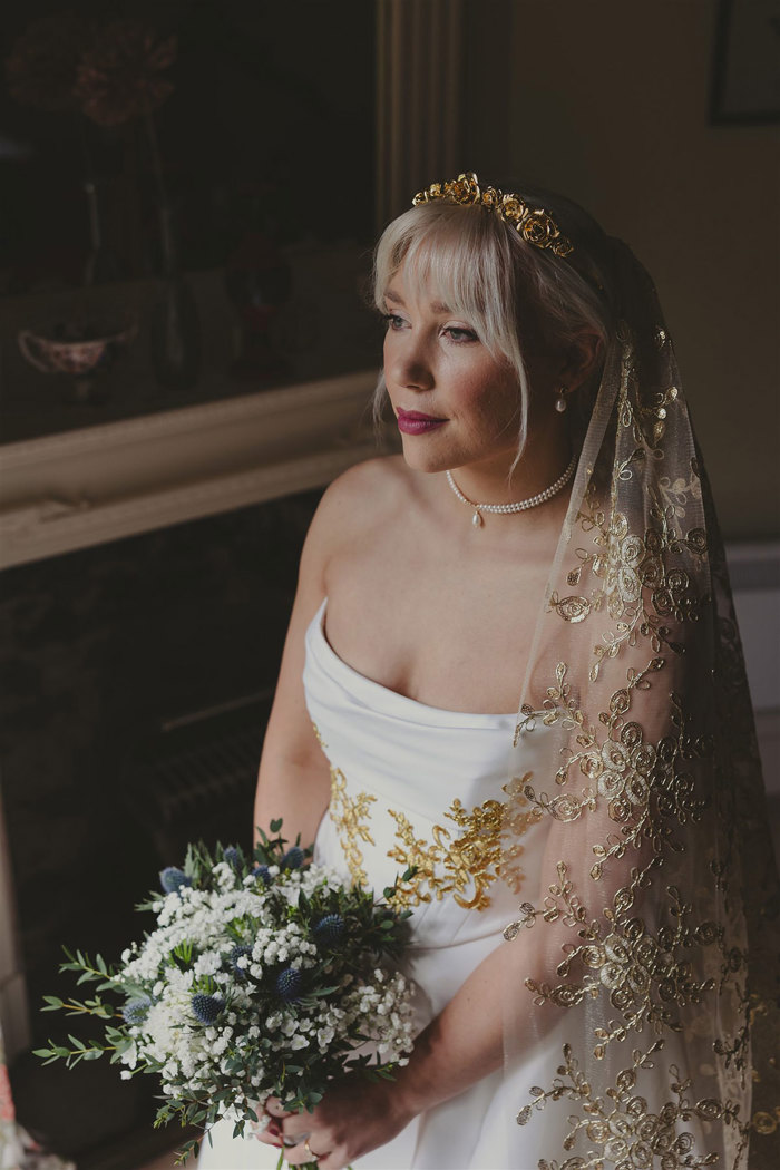 a bride with a gold embroidered veil holding a bouquet of flowers.