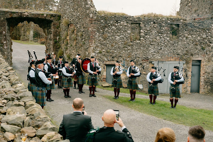 a pipe band performing next to ruined stone building
