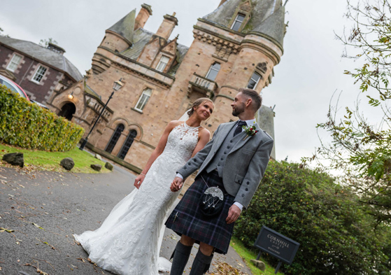 A Bride And Groom Walking With Cornhill Castle In Background