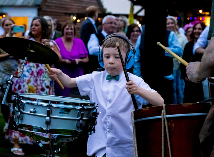 young boy wearing headphones and drumsticks playing drumkit