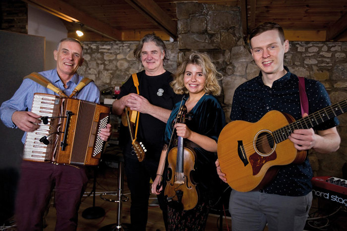 a band of four people holding an accordion, violins and a guitar