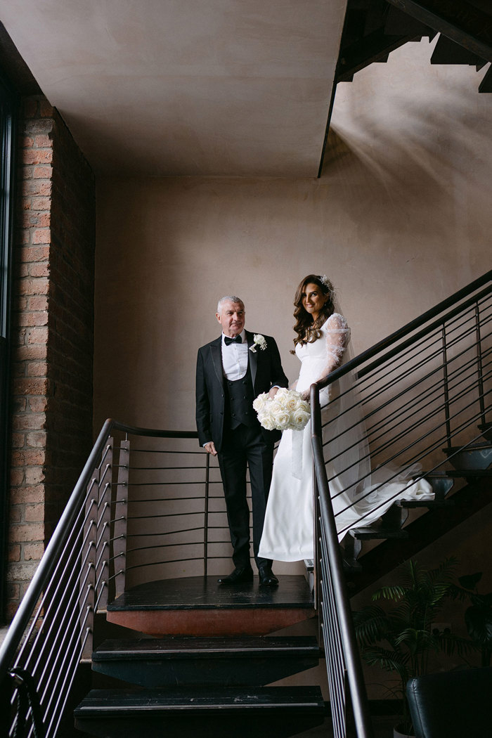 a bride and a man in a suit walking down a staircase at the Engine Works