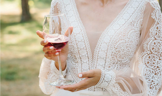 Woman wearing white lace dress holding red wine glass