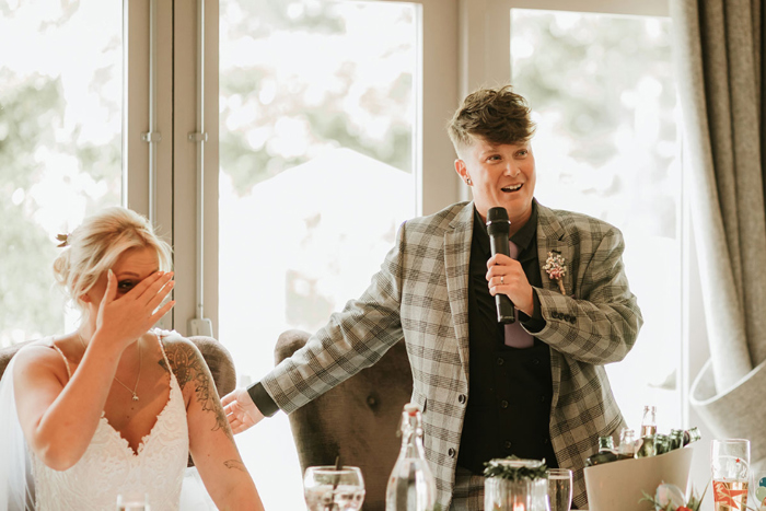 One bride covers face as other talks into a microphone 