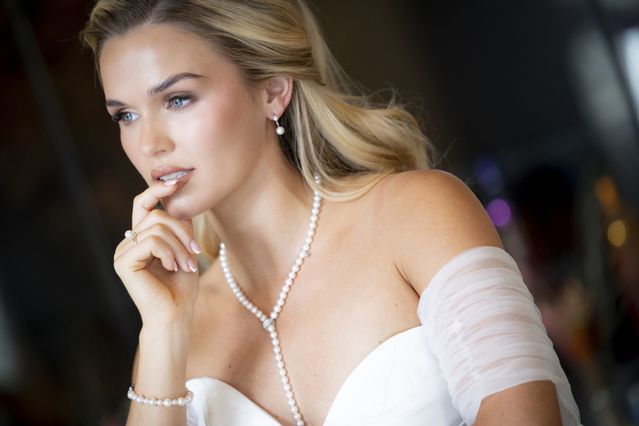 A close up of a woman wearing a white dress and pearl jewellery with her hair pulled back in a half up half down hairstyle