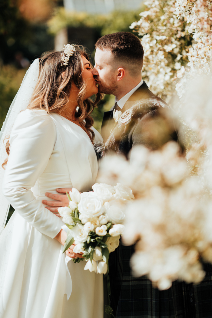 A bride and groom stand outside and share a kiss