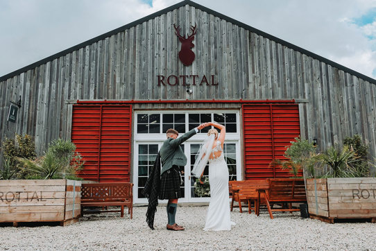 a groom twirling a bride outside the exterior of Rottal Steading