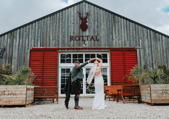 a groom twirling a bride outside the exterior of Rottal Steading