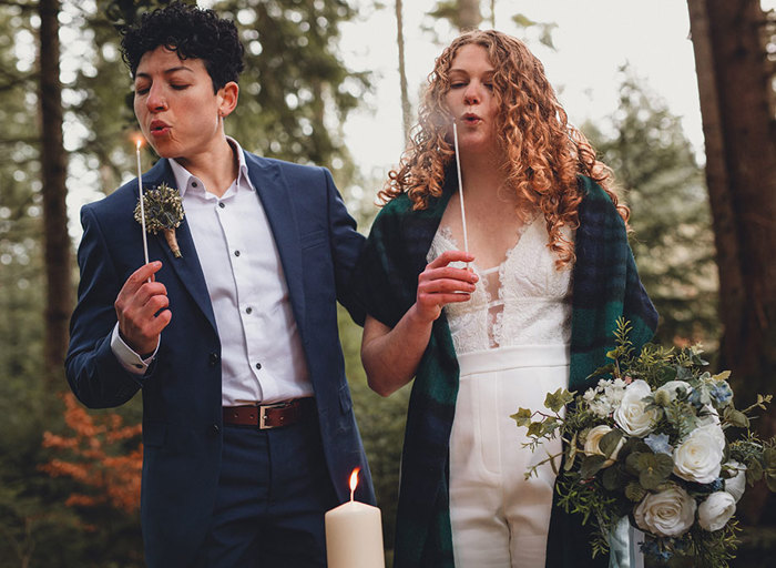 A couple blow out matches after while standing behind a large white pillar candle 