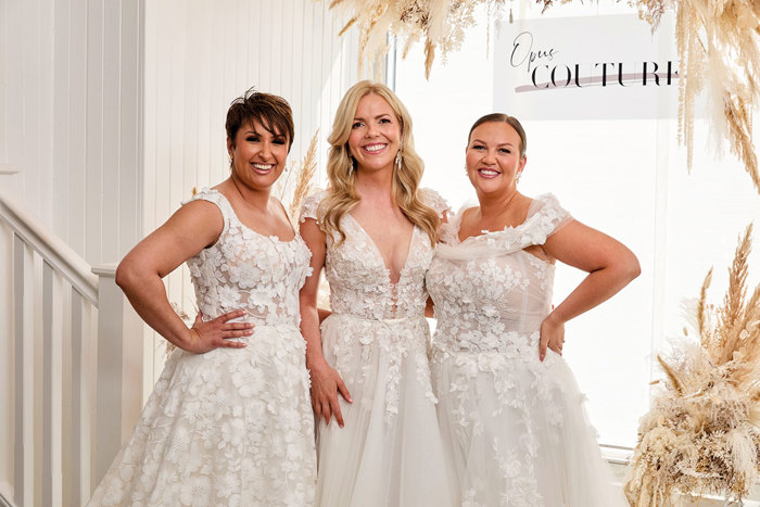 Three women standing in a row wearing wedding dresses at Opus Couture.