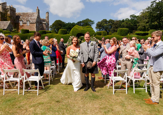 A bride and groom walk down the aisle in between their guests holding hands