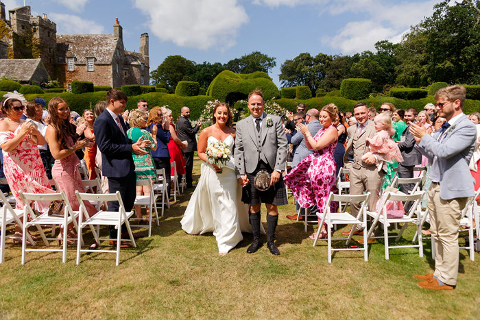 A bride and groom walk down the aisle in between their guests holding hands