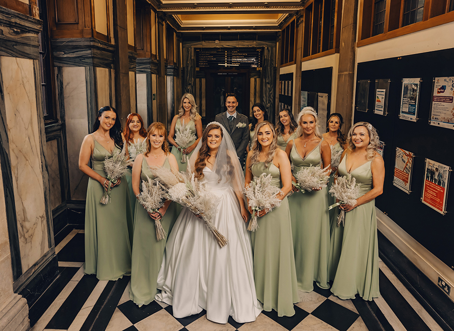 bride wearing white surrounded by bridesmaids wearing sage green standing on black and white floor 