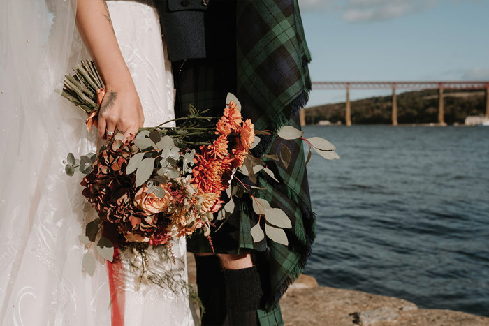 close up of orange bouquet held by a woman standing next to a man by a body of water