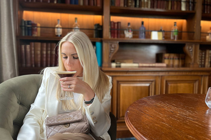 blonde woman sipping espresso martini in a library styled bar