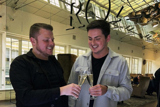 two men clinking champagne flutes in front of a mirror at ROX in Glasgow