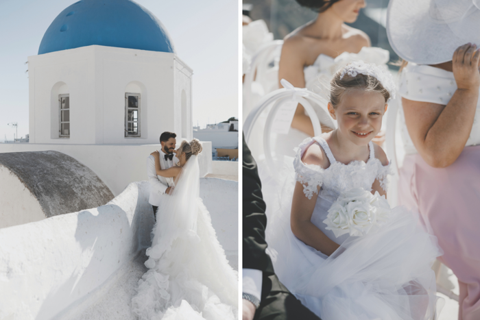 faraway shot of bride with long white train and groom embracing standing in front of blue and white Greek building, young girl sitting down in white dress holding flowers and smiling