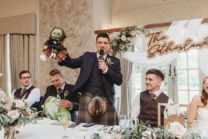 Best man holds doll during wedding speeches