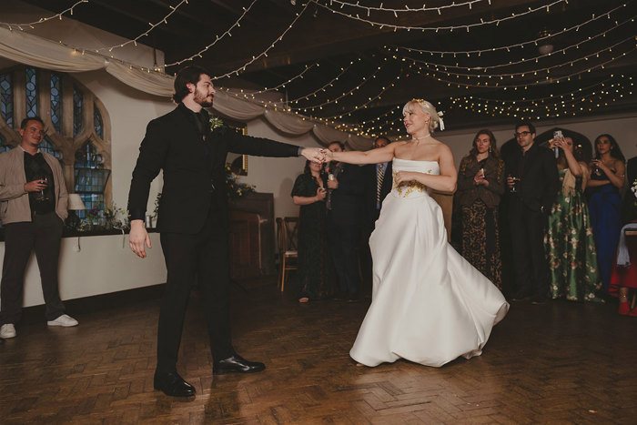 A bride and groom dancing in a room with people watching.