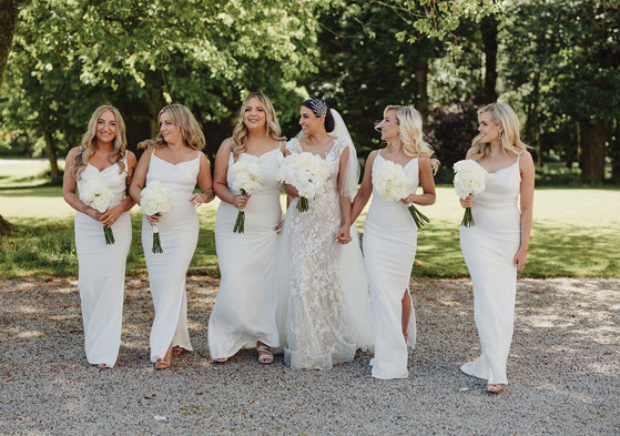 A bride and her five bridesmaids, who are all dressed in white, walk outside (photo: Sam Brill)