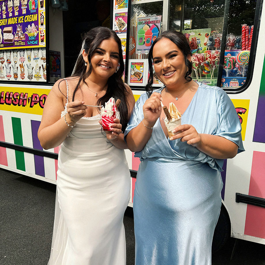 a bride and bridesmaid standing in front of a colourful ice cream van while eating ice cream 