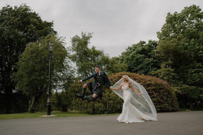 grooms jumps in the air as he holds bride's hand after wedding at cornhill castle