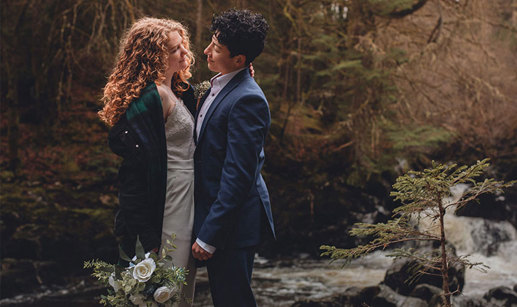 A couple looking into each other's eyes while standing next to a river in a forest